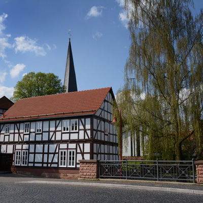 Das Foto zeigt die Dorfbrücke von Bottendorf: Im Vordergrund das Fachwerkgebäude des ehemaligen alten Kindergarten. Hinter dem Dach lugt die Kirchturmspitze hervor.