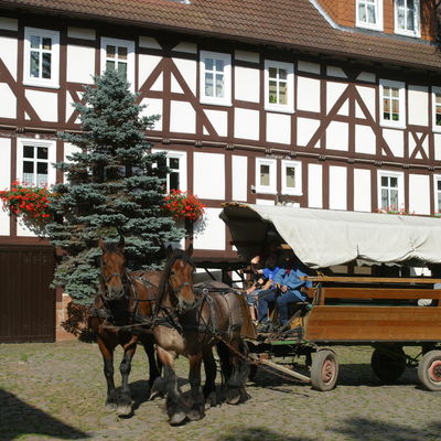 Das Foto zeigt einen Teil des Gebäudes der Linnermühle Bottendorf im Hintergrund, davor ein Kutschengespann mit zwei Pferden und einen Planwagen.