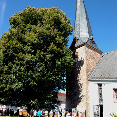 Das Fotozeigt die Ev. Kirche in Bottendorf. Außen vor der geöffneten Eingangstür sitzen Gottesdienstteilnehmer während einem Freiluftgottesdienst.