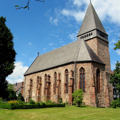 Großansicht der evangelischen Kirche in Wiesenfeld. Davor ist ein Kräutergarten und eine Wiese zu sehen.