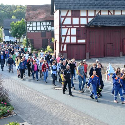 Das Foto zeigt ein Gruppe von ca. 100 Wanderern beim Start des Grenzgangs 2022 in Wiesenfeld. Die Jugendfeuerwehr mit Grenzgangfahne führt die Wandergruppe an. Am Ende folgen drei Reiter zu Pferde.
